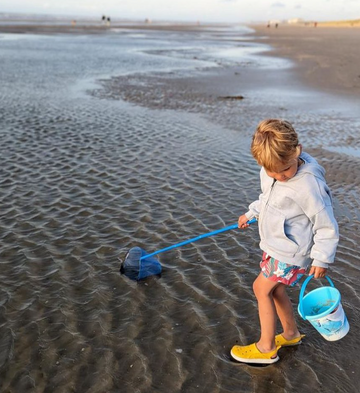 Small child at beach wearing summer clothes and carrying a bucket and a fishing net