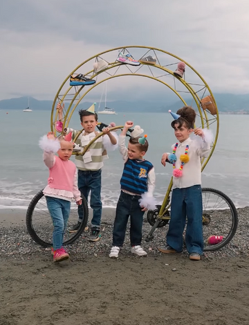 Four children grouped on a beach, a circular construction behind, framing them. beach background, cloudy day