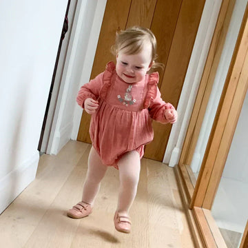 Toddler in pink romper and pink shoes races down a hallway