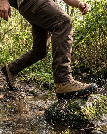 Person striding across a stream in barefoot boots and outdoor gear