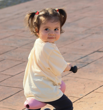 Small Child in yellow tshire looking over shoulder featuring barefoot shoes from Happy Little Soles