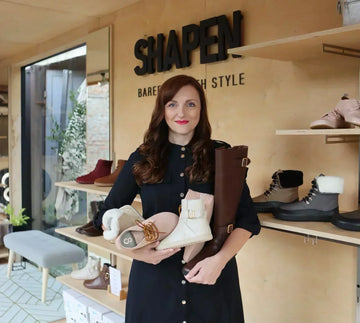 Shapen Founder Mia with her arms full of her barefoot shoes, background is a Shapen store with name above her head.