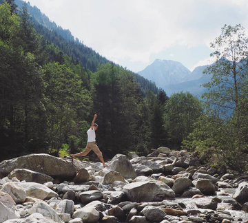 Figure jumping between rocks on dry river bed in mountains with forest background
