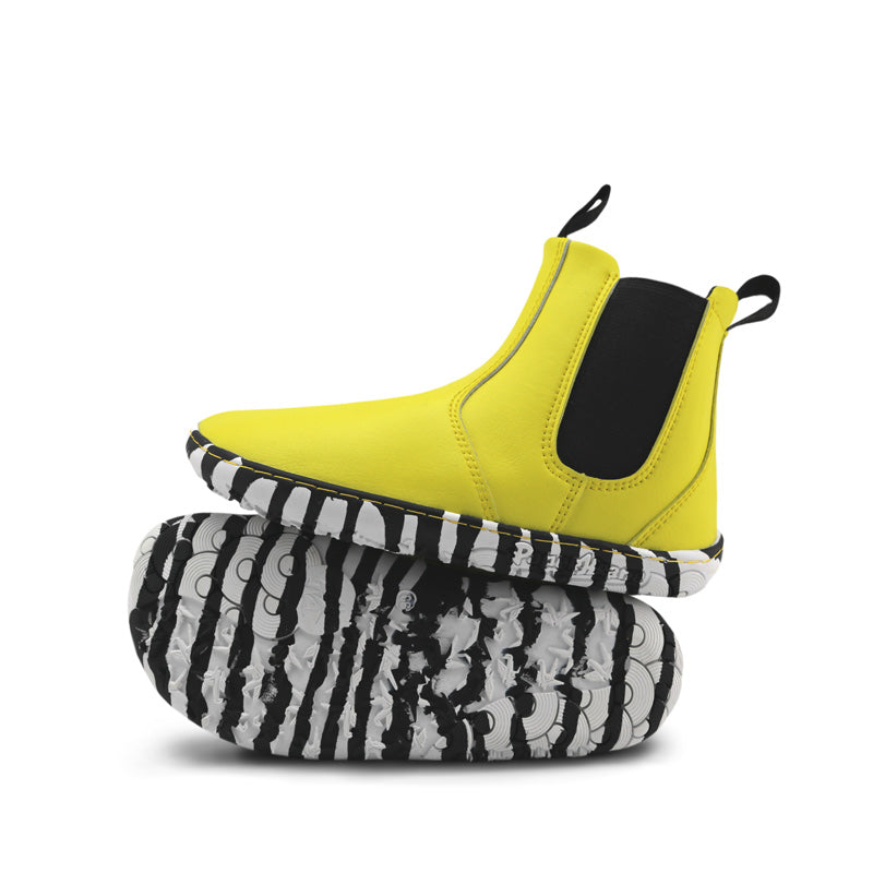 Pair of PaperKrane Kids Sunny Chelsea Boots - Yellow, one balanced on top of the other. One showing the outer side view and the other showing the sole view.