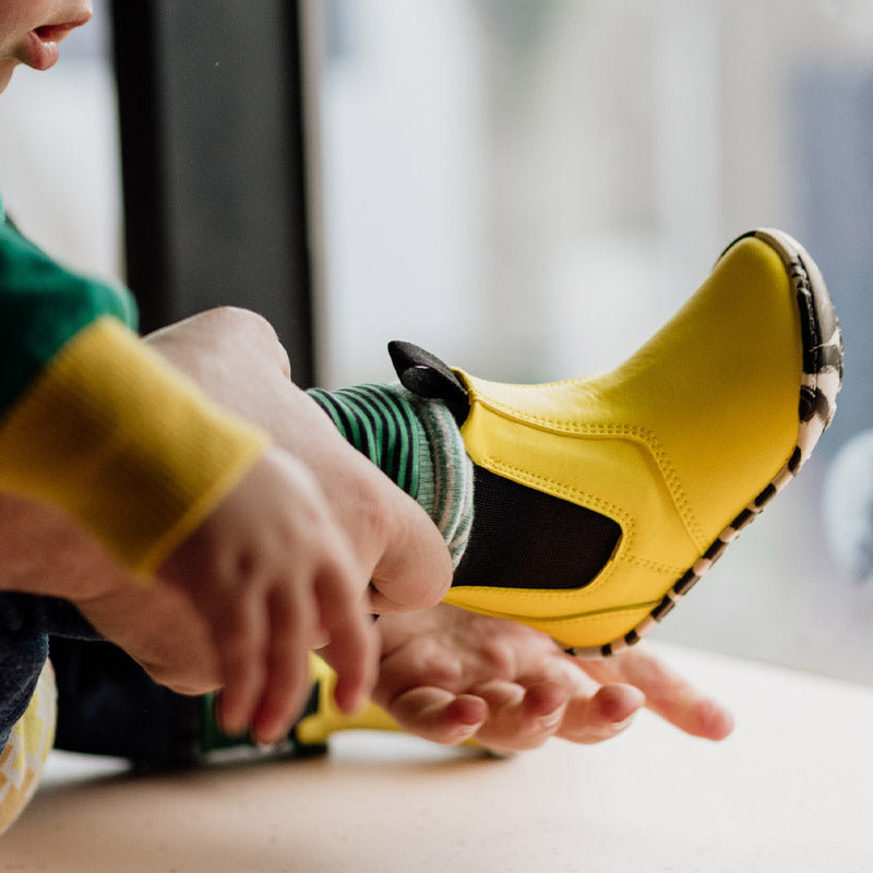 Child being assisted putting on the PaperKrane Kids Sunny Chelsea Boots - Yellow.