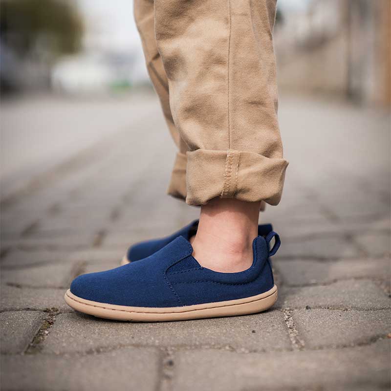 Person wearing Be Lenka Kids Slip-On Shoes Aura - Navy with beige trousers, side view