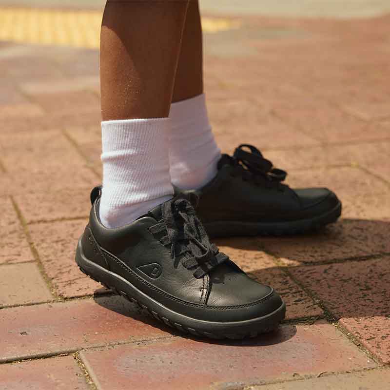 Person wearing Bobux Alpha Evo School Shoes - Black with white socks