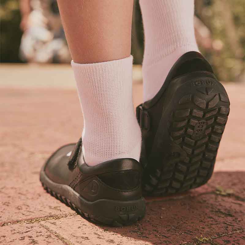 Person wearing Bobux Alpha Hula School Shoes - Black with white socks, rear and sole view