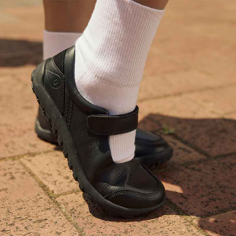 Person wearing Bobux Alpha Hula School Shoes - Black with white socks, outer side view