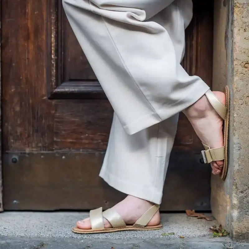 Person wearing Angles Women's Leather Sandals Penelope - Gold with cream trousers