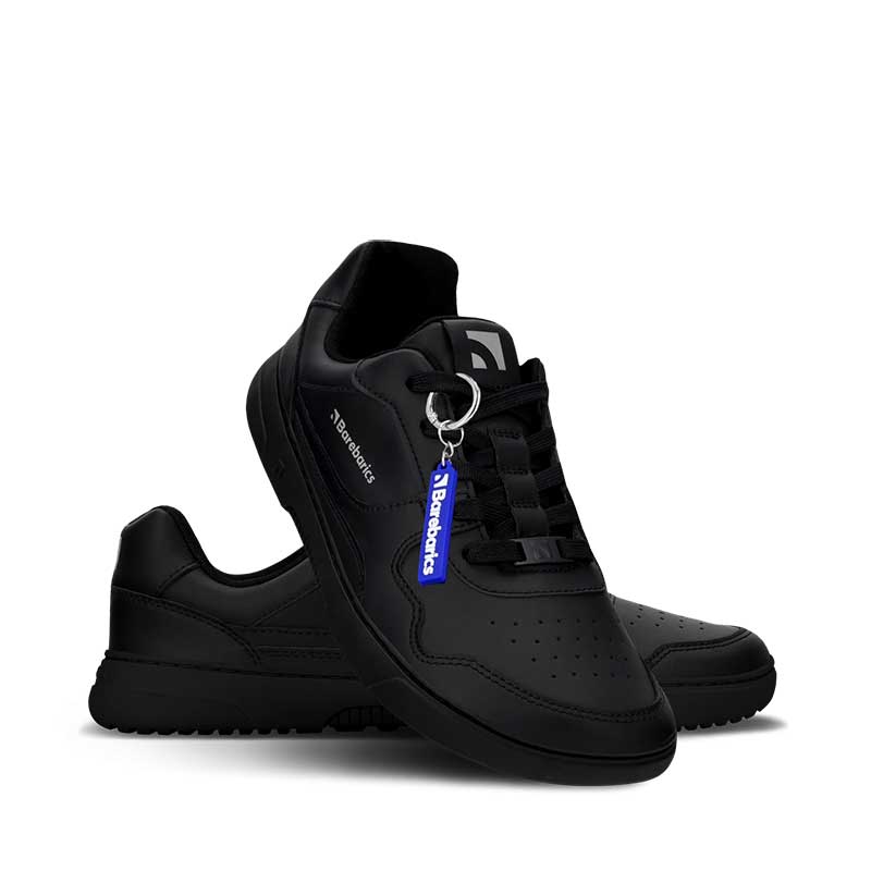 Pair of Be Lenka Adults Barebarics Leather Trainers Zing - All Black, one angled and leaning showing the outer side, the other partially showing the inner side