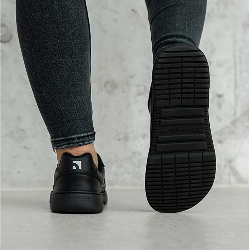 Person is wearing Be Lenka Adults Barebarics Leather Trainers Zing - All Black, showing back and sole of trainers