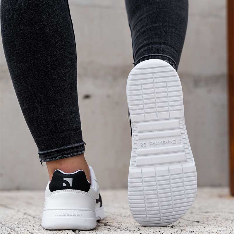 Person wearing Be Lenka Adults Barebarics Leather Trainers Zing - White and Black with black jeans, rear view and sole view