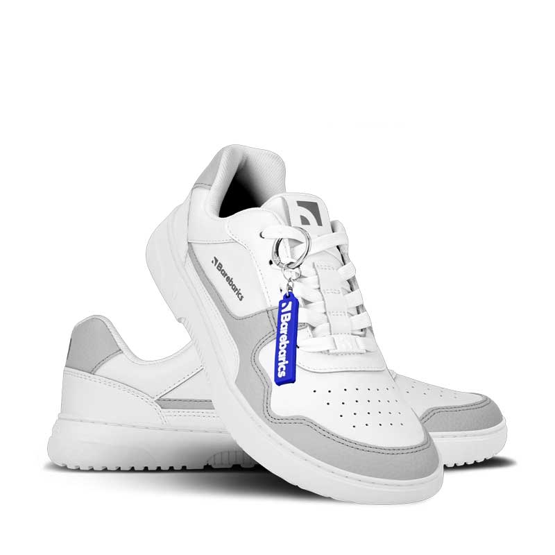Pair of Be Lenka Adults Barebarics Leather Trainers Zing - White and Light Grey, one angled and leaning showing the outer side and Barebarics keyring, the other partially showing the inner side